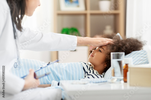 healthcare, medicine and people concept - doctor with clipboard and little sick african american girl lying in bed at home