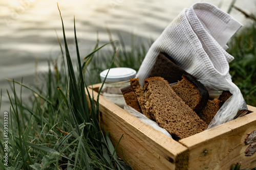 Slices of black bread and a boiled chicken egg on a white towel on the green grass. Picnic in nature with simple food. Next to the salt and flowers with plants in a wooden box.
