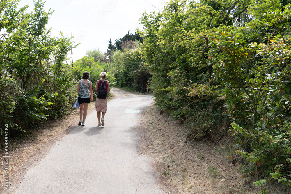 women couple go to beach of isle Noirmoutier by sand pathway in Vendee France women couple go to beach of isle Noirmoutier by sand pathway in Vendee France