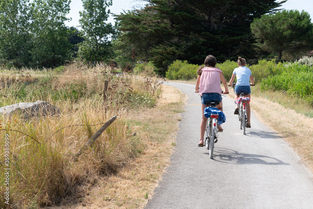 two girls ride bike in path bikeway in Ile de noirmoutier island in France Vendée two girls ride bike in path bikeway in Ile de noirmoutier island in France Vendée