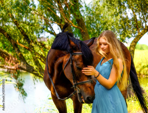 outdoor portrait of young beautiful woman with horse. Against the background of a tree by the river