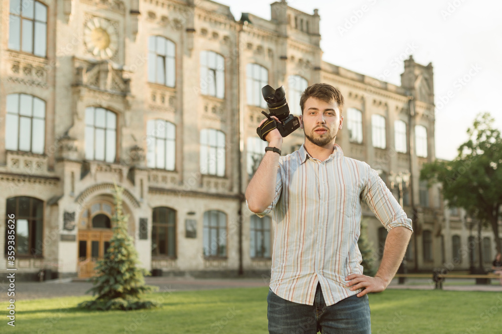 Portrait of bearded man with camera on background of university building, standing on campus and posing for camera. Studying for a photographer at university. Education of a photographer.