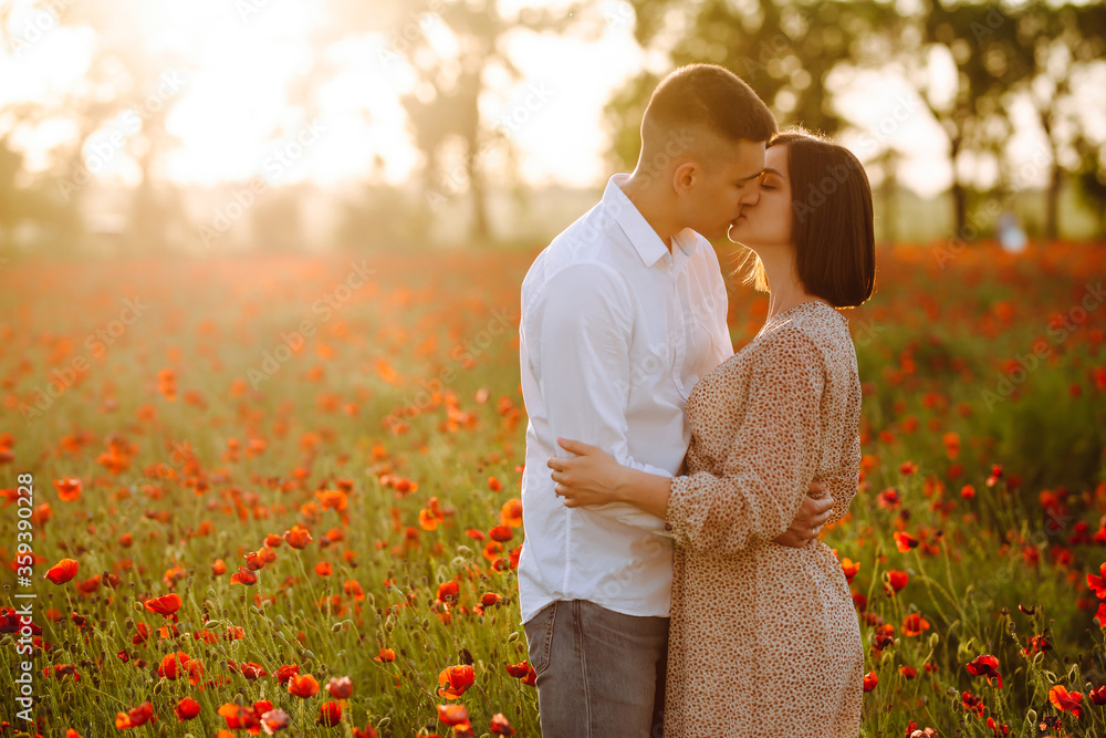 Young romantic loving married couple is standing among the red poppy flowers on the field on the beautiful sunset. Attractive boy and tender girl hug and kiss feeling happy. Love, family concept. Young romantic loving married couple is standing among the red poppy flowers on the field on the beautiful sunset. Attractive boy and tender girl hug and kiss feeling happy. Love, family concept.
