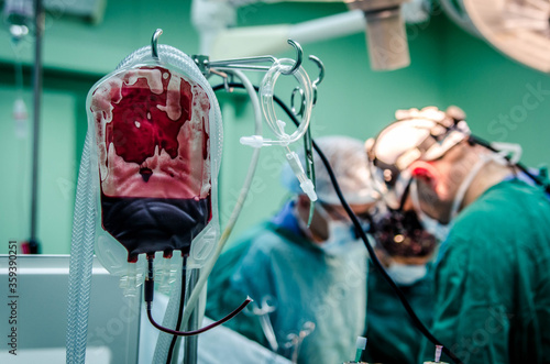 A bag of donated blood used during surgery against a background of a team of surgeons. photo