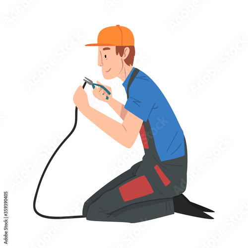Male Electrician Engineer Sitting on His Knee Repairing Cable with Pliers, Electricity Maintenance Service Worker Character in Uniform and Cap Cartoon Style Vector Illustration