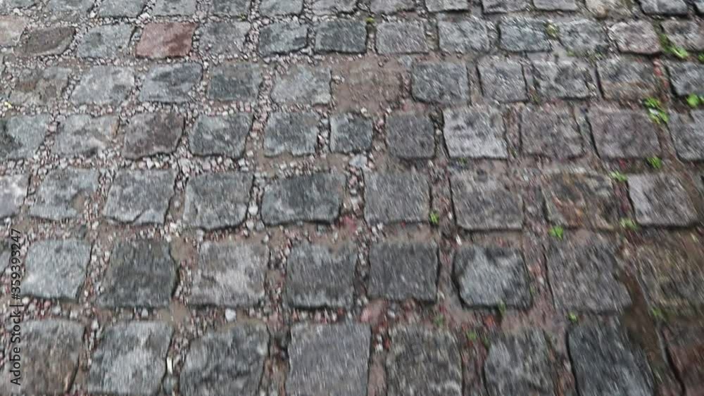A wet sidewalk creates a shiny backdrop. Stone road, paving stones in the old city during the rain during the daytime. Vertical Praming of a First Person Walking Person. A wet sidewalk creates a shiny backdrop. Stone road, paving stones in the old city during the rain during the daytime. Vertical Praming of a First Person Walking Person.