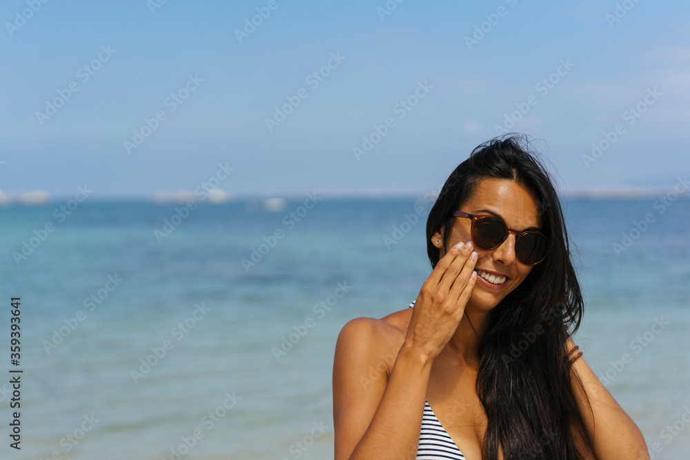 Smiling woman applying sun protection cream on her face in the beach