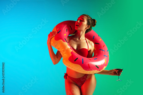 Fashion portrait of seductive girl in swimwear with swim donut on gradient background in neon. Beach season. Woman with sportive body. Resort, vacation, holidays concept. Copyspace. Cocktail party.