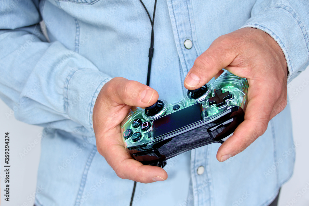 man holds in his hands a black game joystick with green backlight to a modern video game console, the concept of computer games, gaming addiction, hobbies