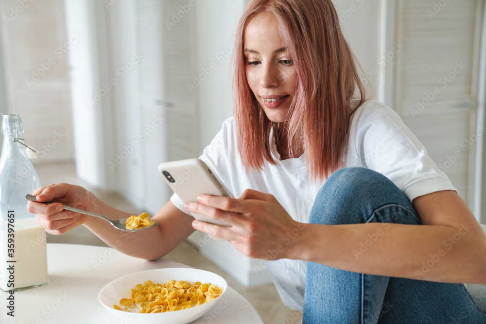 Photo of young caucasian woman using cellphone while having breakfast