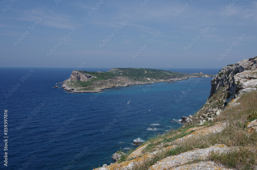 A ridge of the island of San Nicola that falls overhanging the sea and in the background the island of Capraia with its abandoned lighthouse - Tremiti Islands - Adriatic Sea - Italy