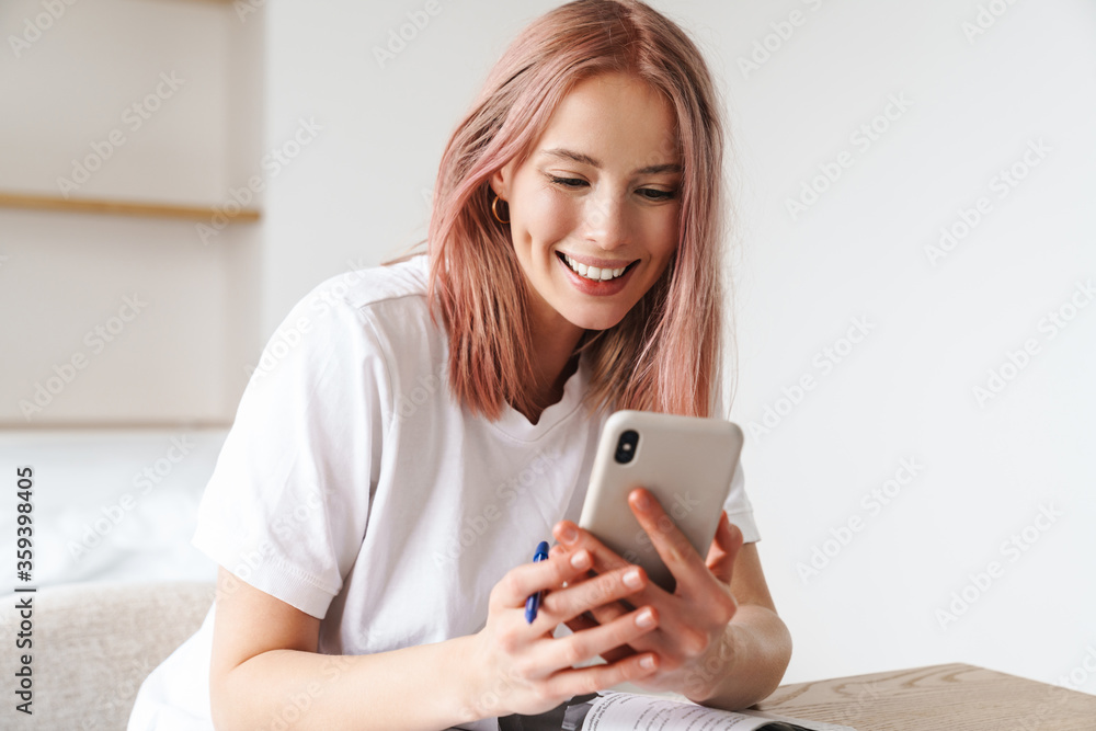Image of woman using smartphone while doing homework with exercise books Image of woman using smartphone while doing homework with exercise books