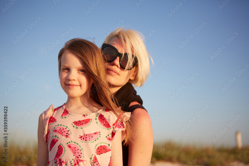 Smiling mother and beautiful daughter having fun on the beach. Portrait of happy woman giving a piggyback ride to cute little girl with copy space. Portrait of kid embracing her mom during summer. Smiling mother and beautiful daughter having fun on the beach. Portrait of happy woman giving a piggyback ride to cute little girl with copy space. Portrait of kid embracing her mom during summer.