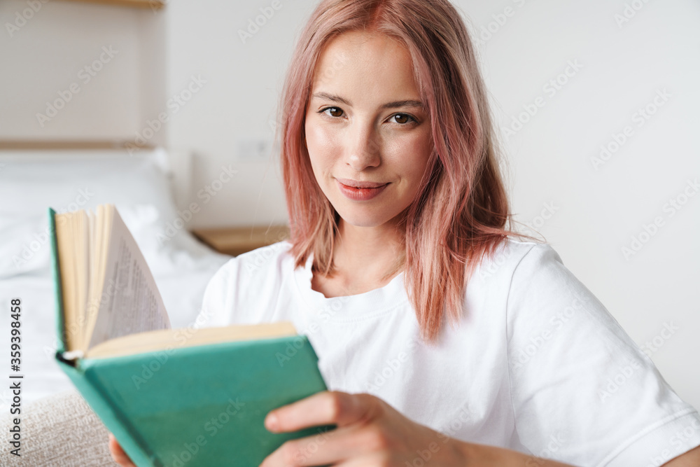 Image of pleased pretty woman with pink hair reading book and smiling Image of pleased pretty woman with pink hair reading book and smiling