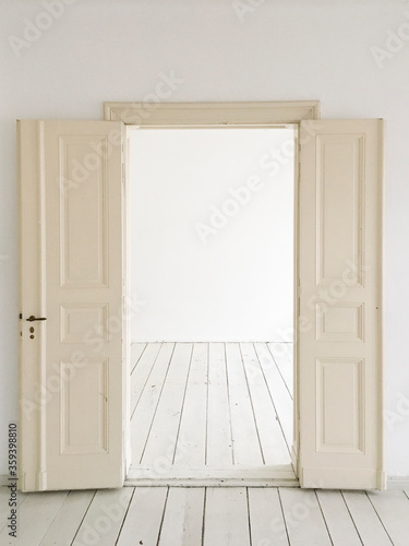 Old white doors leading into a white space. Empty rooms with white walls and white floors.