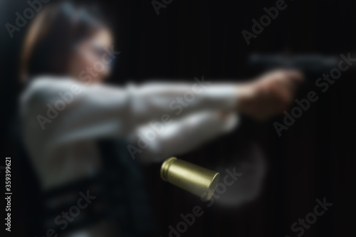 Flying bullet shells with Woman wearing bulletproof vest shoots with gun at a target at indoor gun range.