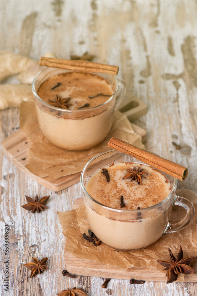Glass cups of traditional Indian masala chai on light wooden background. Ingredients of beverage black tea, ginger, cinnamon, cardamom, anise stars Glass cups of traditional Indian masala chai on light wooden background. Ingredients of beverage black tea, ginger, cinnamon, cardamom, anise stars