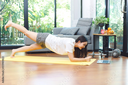 Asian woman searching and watching online tutorials videos on laptop for doing yoga plank, fitness exercise training at home.;