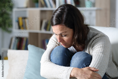 Pensive sad adult woman looking down at home