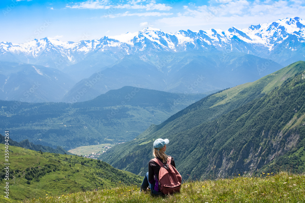A young girl with a backpack sits on the top of a mountain in Georgia and contemplates the landscape. The traveler made the climb. Hiker relax and looking over horizon.