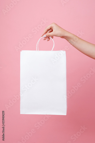 white paper bag under the logo in the hands of the girl on a pink background. Shopping mock up holding