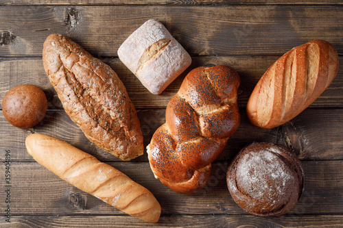 Variety of loaves of bread and buns on wooden table background.