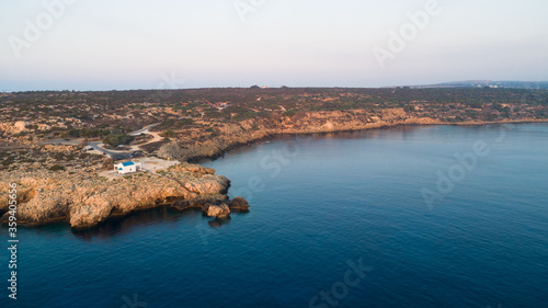 Aerial bird’s eye view of coastline landmark white washed chapel Agioi Anargyroi, Cavo Greco Protaras, Famagusta, Cyprus from above. Tourist attraction cliff Ayioi Anargiroi church, caves at sunrise. photo