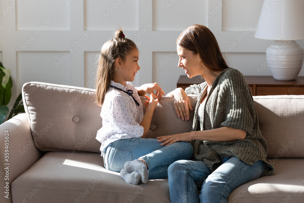 Caring mother and little daughter chatting, sitting on cozy couch in living room, pretty girl sharing secrets with loving mum, having pleasant conversation, good trusted family relationship Caring mother and little daughter chatting, sitting on cozy couch in living room, pretty girl sharing secrets with loving mum, having pleasant conversation, good trusted family relationship