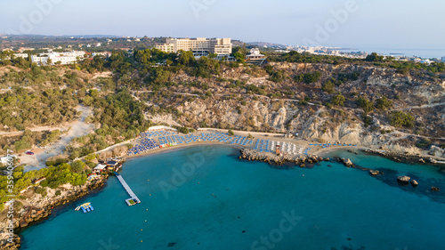 Fototapeta Naklejka Na Ścianę i Meble -  Aerial bird's eye view of Konnos beach in Cavo Greco Protaras, Paralimni, Famagusta, Cyprus. The famous tourist attraction golden sandy Konos bay, yachts, on summer holidays, at sunrise from above