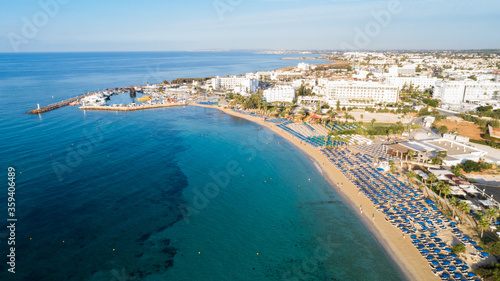Aerial bird's eye view of Pantachou - Limanaki beach (Kaliva), Ayia Napa, Famagusta, Cyprus. Bay with golden sand, small fishing port, sunbeds, parasols, sea bar restaurants in Agia Napa, from above.