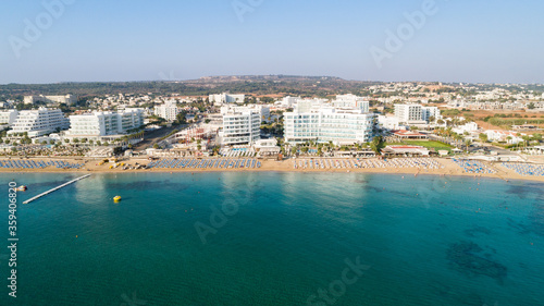 Fototapeta Naklejka Na Ścianę i Meble -  Aerial bird's eye view of Sunrise beach Fig tree, Protaras, Paralimni, Famagusta, Cyprus.The famous tourist attraction family bay with golden sand, boats, sunbeds, restaurants, water sports from above