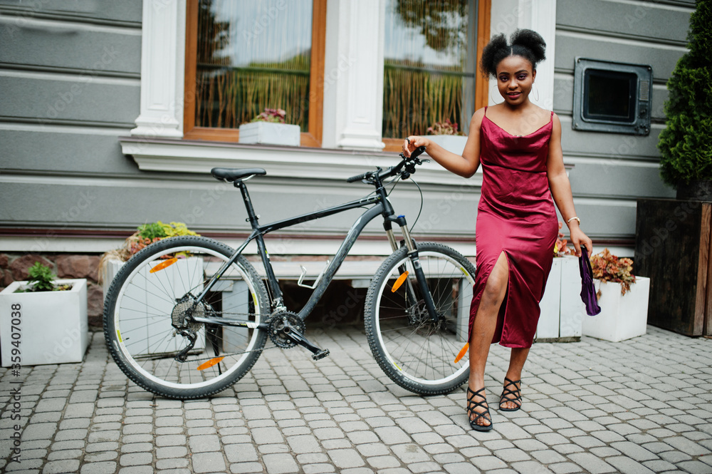 Portrait of a beautiful natural young African woman with afro hair. Black model in red silk dress with mountain bike.