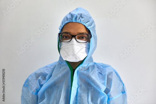 Portrait of a female medical health professional wearing a blue hazmat suit (PPE) and white N95 mask isolated on grey background