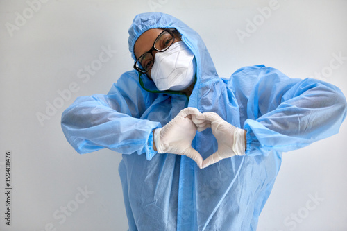 Lady medical professional wearing a blue hazmat suit (PPE), white N95 mask and white surgical gloves makes the heart sign- isolated on white background