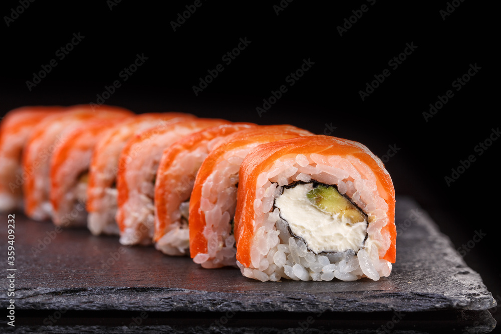 Philadelphia sushi rolls with salmon and cream cheese and avocado on a black slate plate close up. Philadelphia sushi rolls with salmon and cream cheese and avocado on a black slate plate close up.