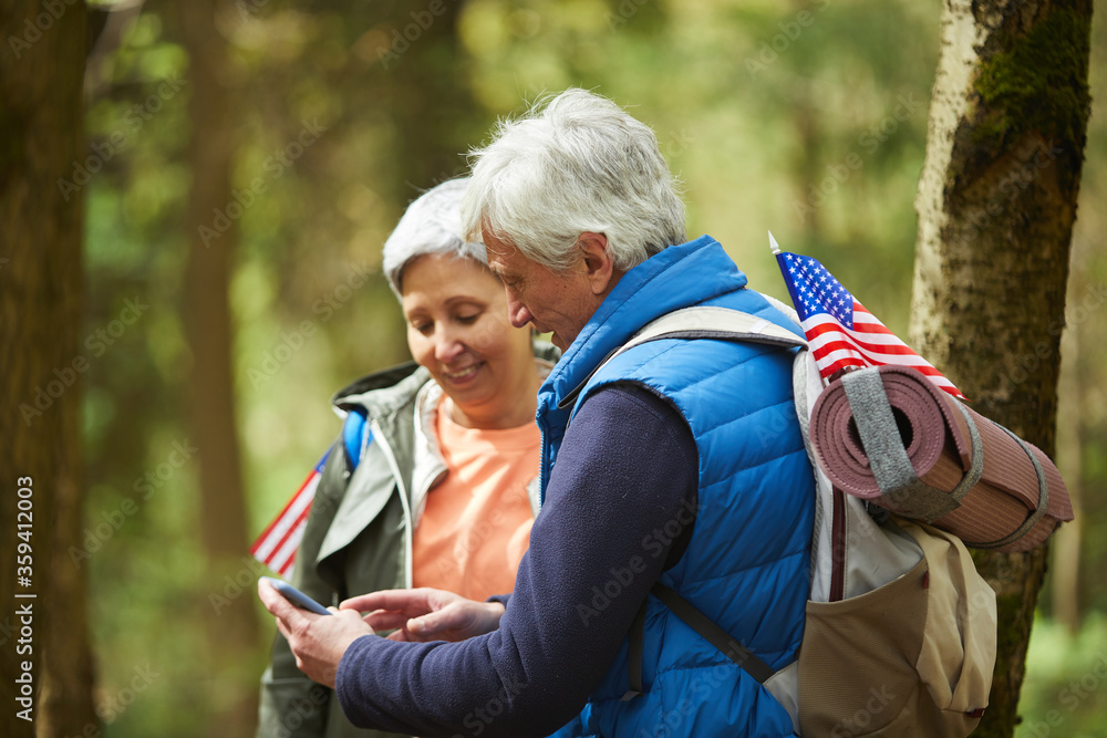 Side view at active senior couple using mobile app via smartphone while enjoying hike in forest, copy space Side view at active senior couple using mobile app via smartphone while enjoying hike in forest, copy space