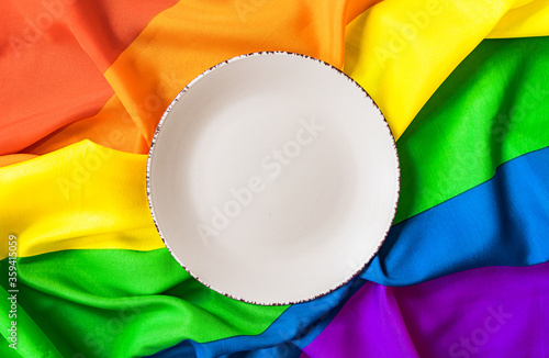 White plate on the background of a rainbow LGBT symbol close - up for design. Lunch dish on a rainbow background.