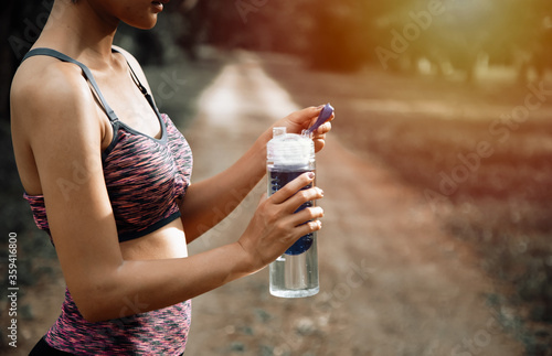 Female runner standing outdoors holding water bottle,  healthy and sport concept.