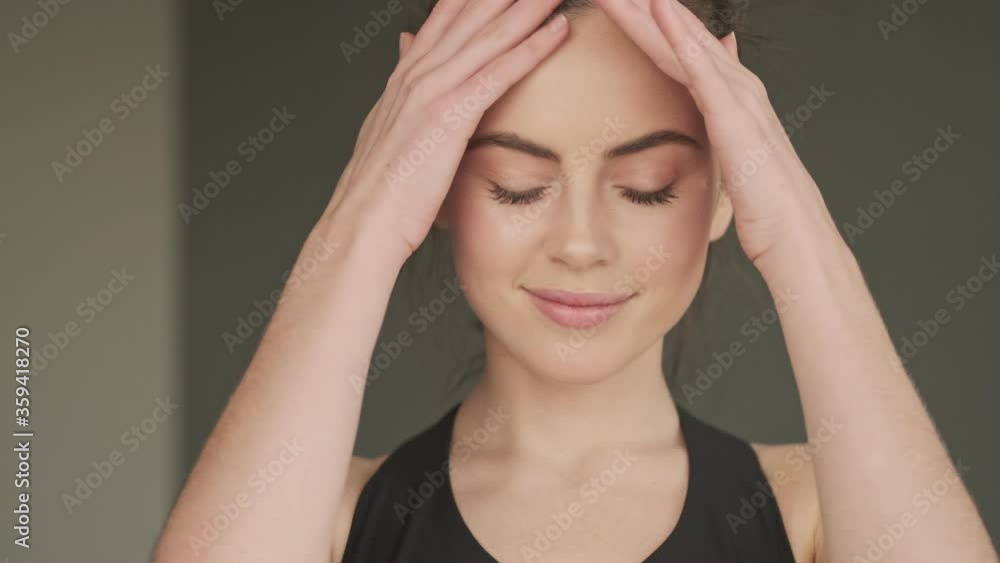 A close-up view of a nice happy young woman is posing to the camera in a gray studio A close-up view of a nice happy young woman is posing to the camera in a gray studio