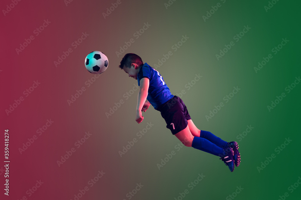 Teen male football or soccer player on gradient background in neon light. Caucasian expressive boy training, practicing on the run, in jump. Concept of sport, competition, winning, motion, action.