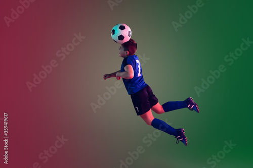 Teen male football or soccer player on gradient background in neon light. Caucasian expressive boy training, practicing on the run, in jump. Concept of sport, competition, winning, motion, action.