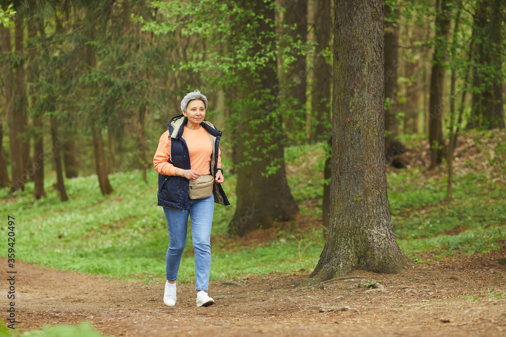 Full length portrait of active senior woman running while enjoying hike in beautiful autumn forest, copy space Full length portrait of active senior woman running while enjoying hike in beautiful autumn forest, copy space