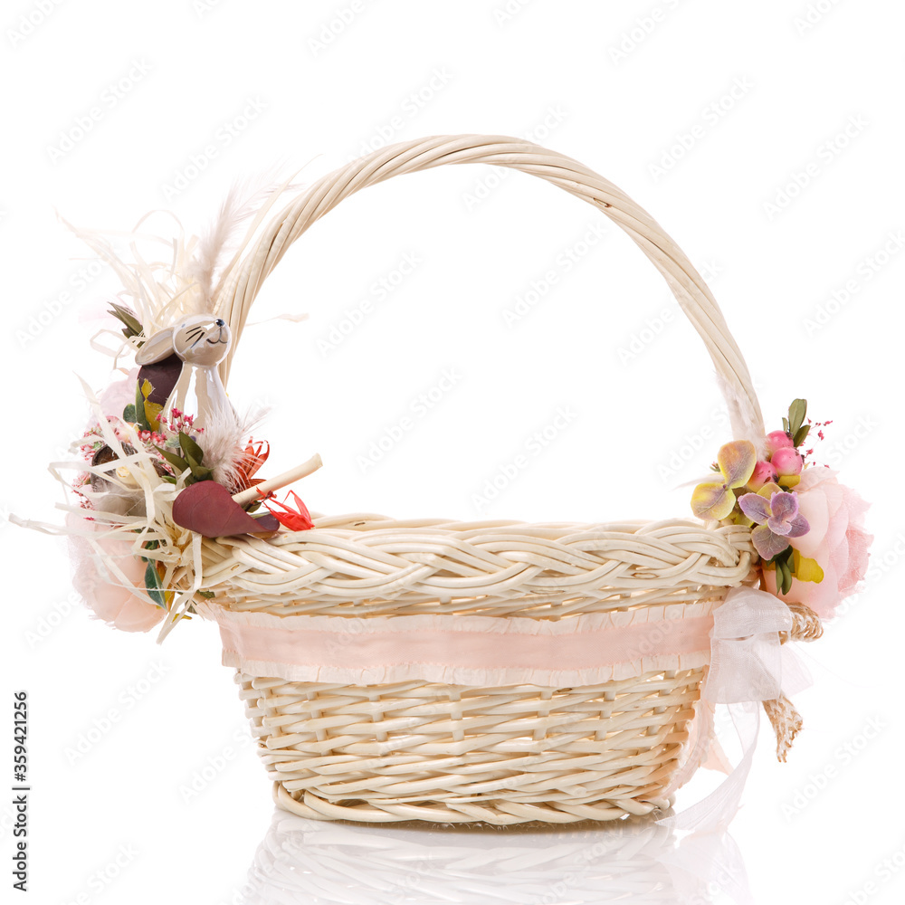 Wicker basket of natural vines with floral decor and ribbons on white background. The basket decor is made in delicate pink tones for Easter celebration.
