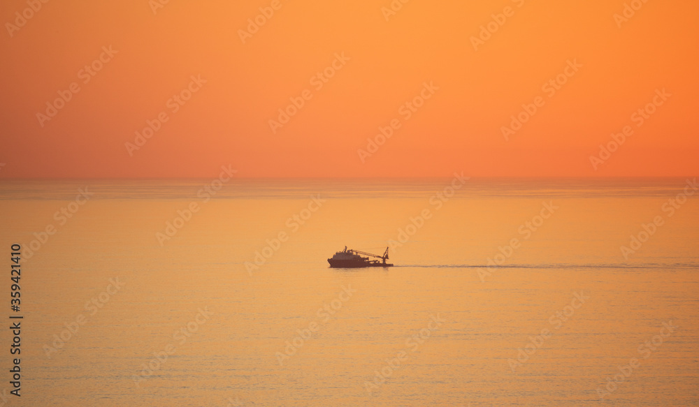 Naklejka premium Fishing boat sailing across Camps Bay in golden orange sunset light.
