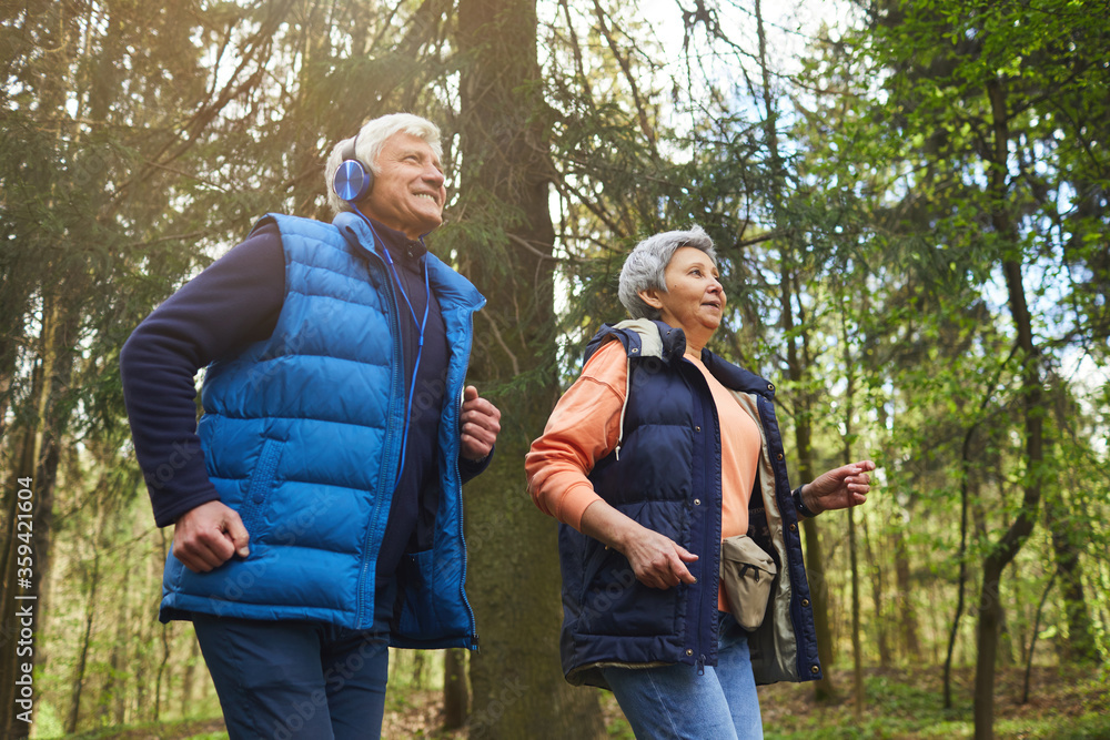Low angle portrait of active senior couple enjoying morning run in beautiful green forest, copy space Low angle portrait of active senior couple enjoying morning run in beautiful green forest, copy space