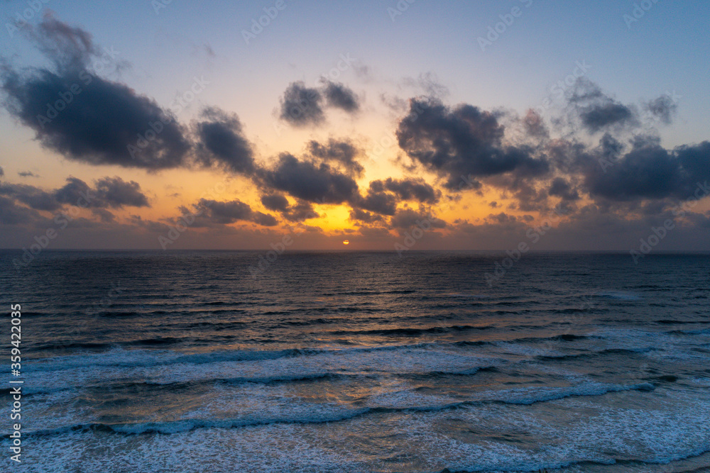 Beautiful sunset with dark blue sky and orange golden colors sun over the sea with dramatic clouds in the sky and waves close to the beach shore concept of romantic time on vacation