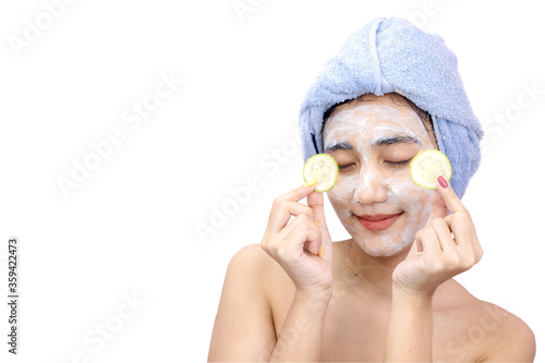 The beauty of a happy Asian woman wearing a yogurt mask mixed with lemon juice and holding a cucumber in her hand on a white background.