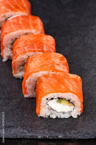 Philadelphia sushi rolls with salmon and cream cheese and avocado on a black slate plate close up.