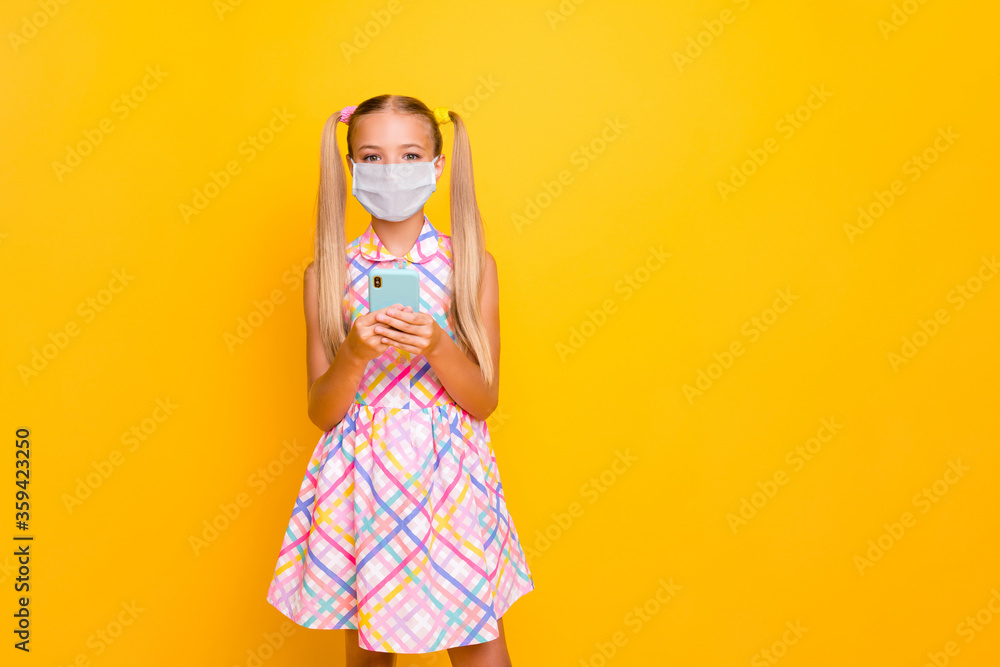 Portrait of her she nice lovely healthy little lady wearing safety mask dress using device gadget browsing mers cov news prevention isolated bright vivid shine yellow color background