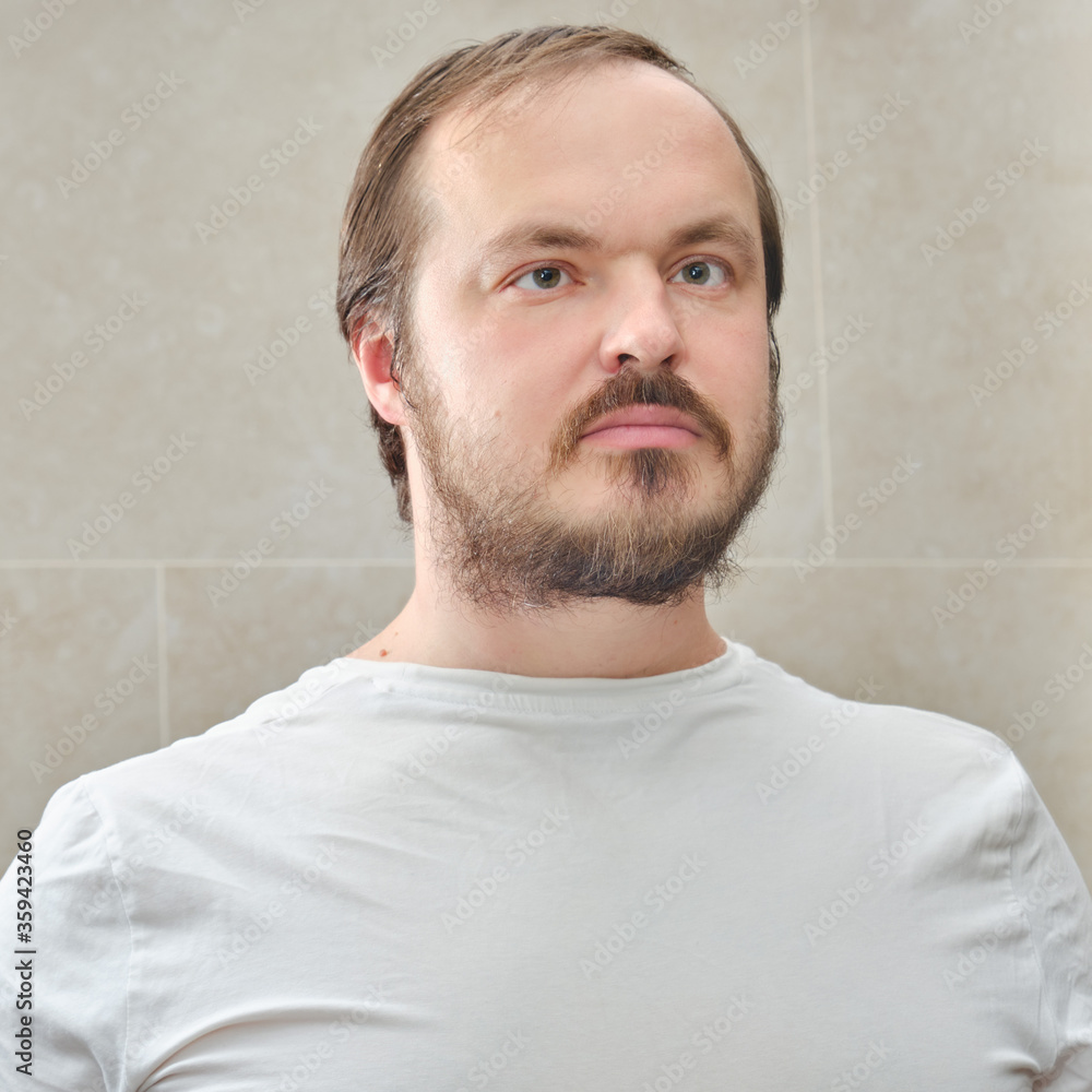 Obraz premium Portrait of a man with a beard in a white t-shirt, close-up. Face of a man 35-40 years old on a beige background